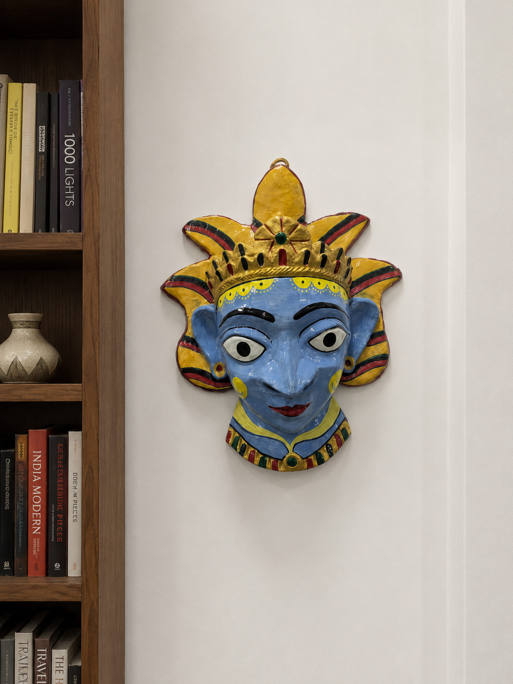 A hand-painted papier mache wall mask of a stylized face with a crown, mounted on a white wall.